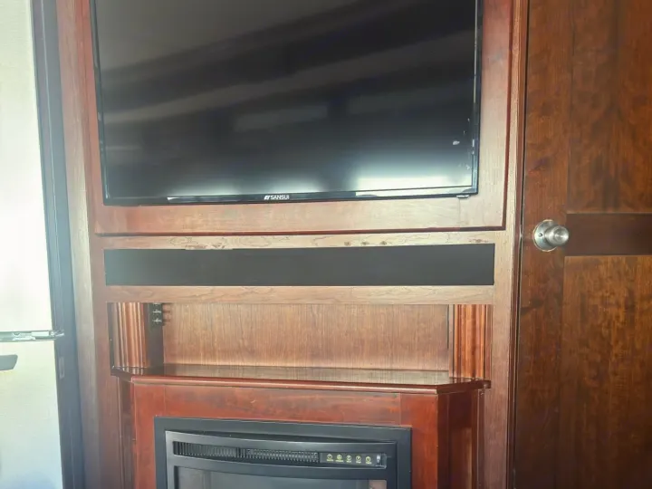 RV rental interior: Dark wood entertainment unit featuring a Sansui TV, black media shelf, and electric fireplace.. Fleetwood 35 K 2017