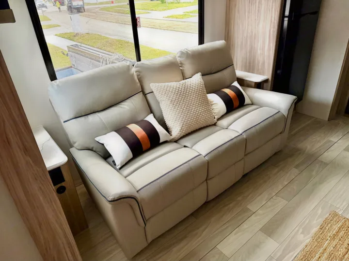 Relaxing RV rental living area featuring a modern recliner sofa, stylish pillows, and light wood flooring.. Winnebago Access 2024