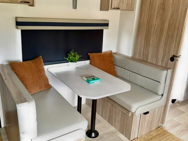 Cozy RV rental dinette featuring bench seating, a marble-patterned table, and accent pillows. Ideal for dining and games on your travels.. Winnebago Access 2024