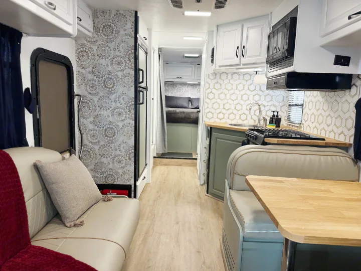 Bright RV rental interior showcasing a modern kitchen, cozy sofa, and bedroom. Features light wood floors and stylish patterned wallpaper.. Thor Majestic 2014