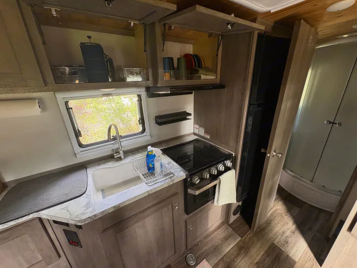 Inside an RV rental: A bright, functional kitchen with a sink, stove, refrigerator, and overhead storage cabinets.. Imperial Outdoors XploreRV 2022