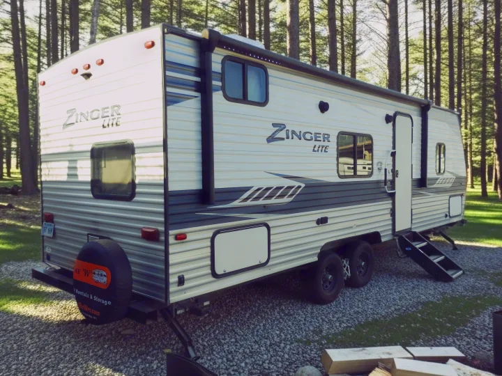 This Zinger Lite travel trailer is ready for your next rv rental adventure, parked on gravel in the woods.. Crossroads RV Zinger Lite 2020