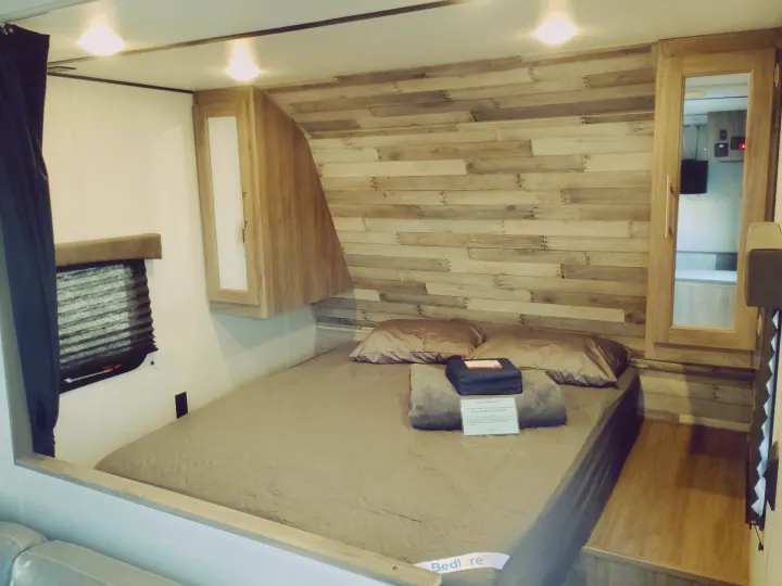 Step into this cozy RV rental bedroom, featuring a comfortable bed, stylish wood accent wall, and practical storage.. Crossroads RV Zinger Lite 2020