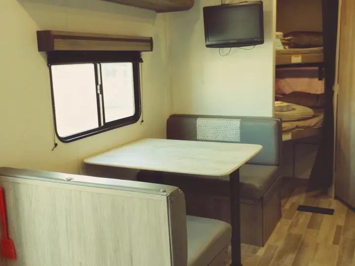 RV rental interior: a cozy dinette with table & bench seats, wall-mounted TV, and bunk beds visible in the background.. Crossroads RV Zinger Lite 2020