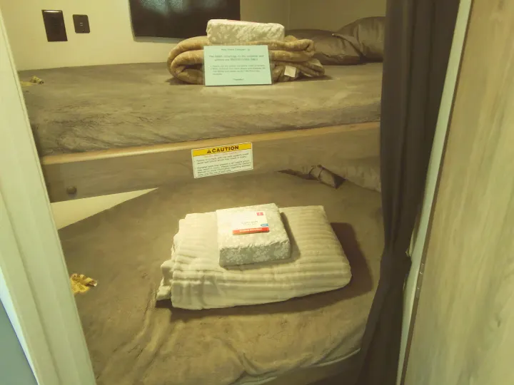 RV rental bunk beds with fresh bedding, a sheet set, and important caution signs about bed capacity and safety.. Crossroads RV Zinger Lite 2020