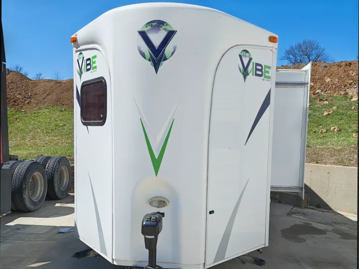 White 'The Vibe' RV rental trailer by V-Cross, with prominent V-shape & globe logos. Parked outdoors.. Forest River V-Cross Vibe 2012