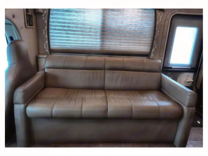 Experience comfort in this RV rental's interior, featuring a taupe sofa, window with blinds, and side door.. Thor Chateau 2020