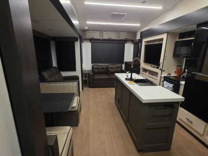 Spacious RV rental interior showcasing a dark sofa, dining area, and a bright kitchen island with modern appliances.. Forest River Cherokee Alpha Wolf 2026