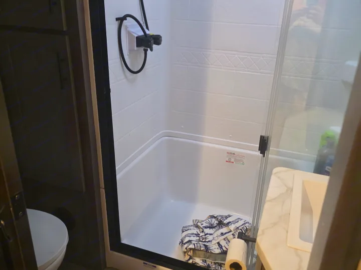 Compact RV rental bathroom showing shower, toilet, and sink. A shirt and toilet paper are in the shower base.. Forest River Cherokee Alpha Wolf 2026