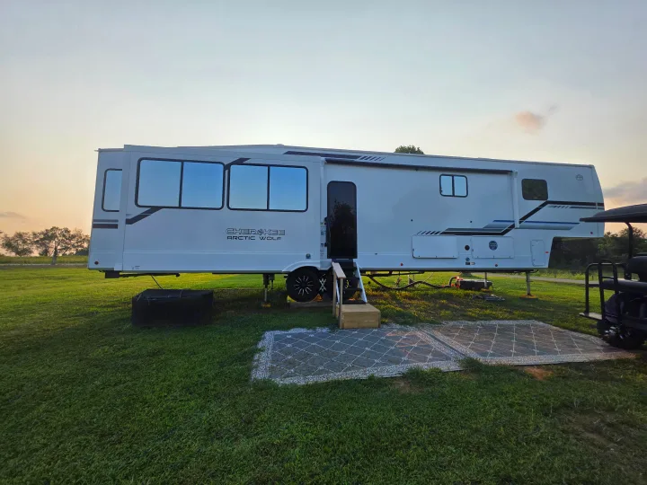 Spacious white Cherokee Arctic Wolf RV rental set up on a grassy campsite with steps and an outdoor rug, ready for adventure.. Forest River Cherokee Alpha Wolf 2026
