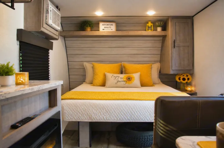 Cozy RV rental bedroom with bright yellow bedding, sunflower decor, and a cheerful "Adventure Awaits" sign.. Keystone RV Coleman Lantern 2025