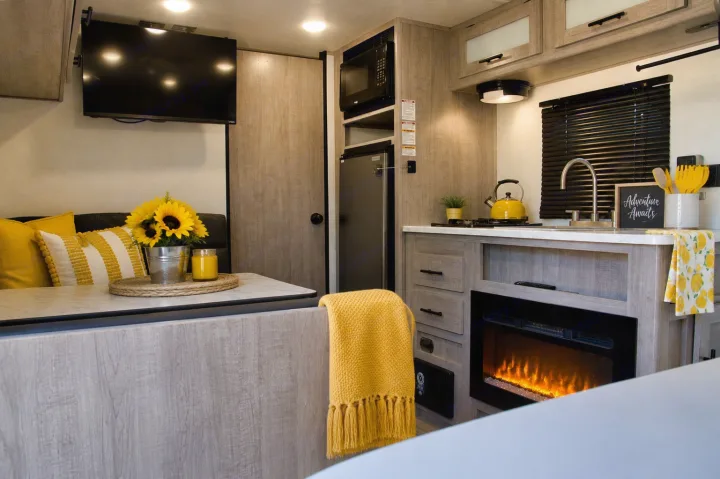 Cozy RV rental interior with kitchenette, dining area, and electric fireplace, featuring bright yellow decor.. Keystone RV Coleman Lantern 2025