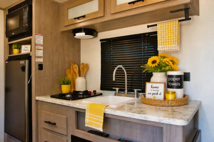 Bright and functional RV rental kitchen, equipped with microwave, fridge, stove, sink, and vibrant yellow decor.. Keystone RV Coleman Lantern 2025