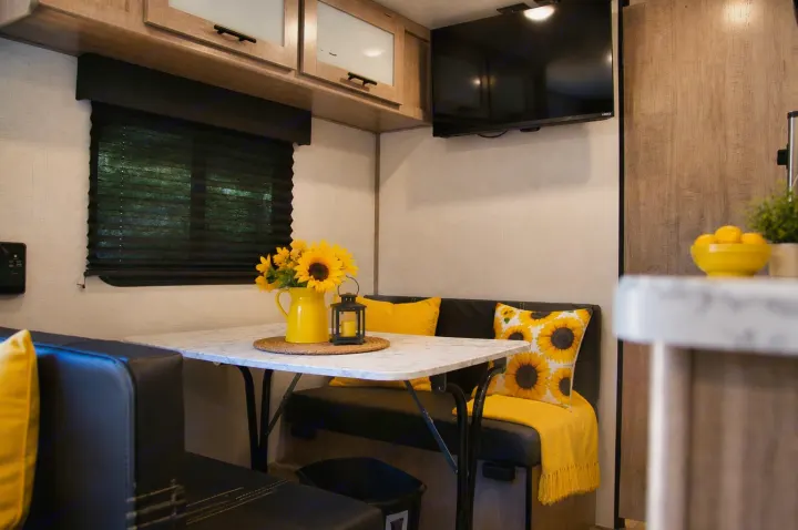 Cozy RV rental dinette with a white table, black benches, and cheerful sunflower decor in a bright and inviting interior.. Keystone RV Coleman Lantern 2025