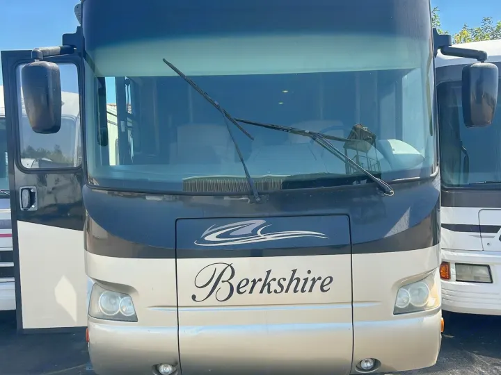 Front view of a tan and black Berkshire motorhome, great for rv rental. Features large windshield, wipers, side mirrors, and an open door.. Forest River Berkshire 2011