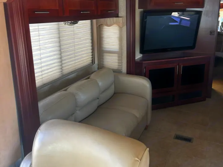 Spacious RV rental living area featuring a comfy sofa, entertainment unit with TV, wood cabinets, and blinds.. Forest River Berkshire 2011