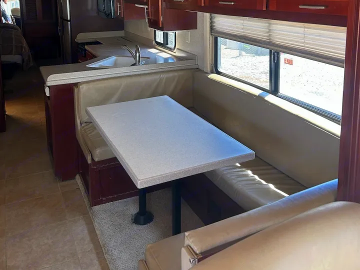 This RV rental features a cozy dinette with bench seating and table, alongside a compact kitchen area.. Forest River Berkshire 2011