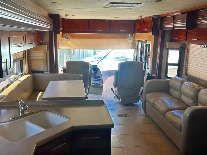 Bright rv rental interior features a kitchen sink, dinette booth, comfy sofa, and front cabin with driver's seats.. Forest River Berkshire 2011