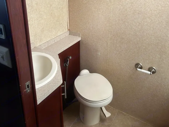 Compact RV rental bathroom: toilet, sink, bidet sprayer, toilet paper holder, and wood cabinetry.. Forest River Berkshire 2011
