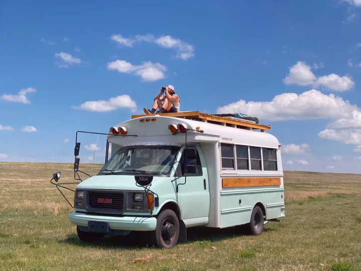 Mint GMC skoolie with a man on the roof using binoculars in a sunny field, ideal for RV rental adventures.. Gmc Savanna 2001