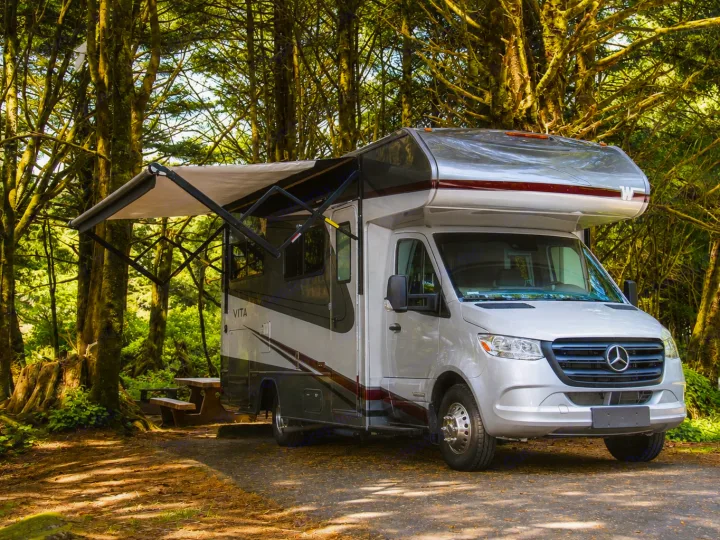 Silver Mercedes-Benz RV rental parked in a lush forest campsite with an extended awning, ready for adventure.. Winnebago Vita 2020