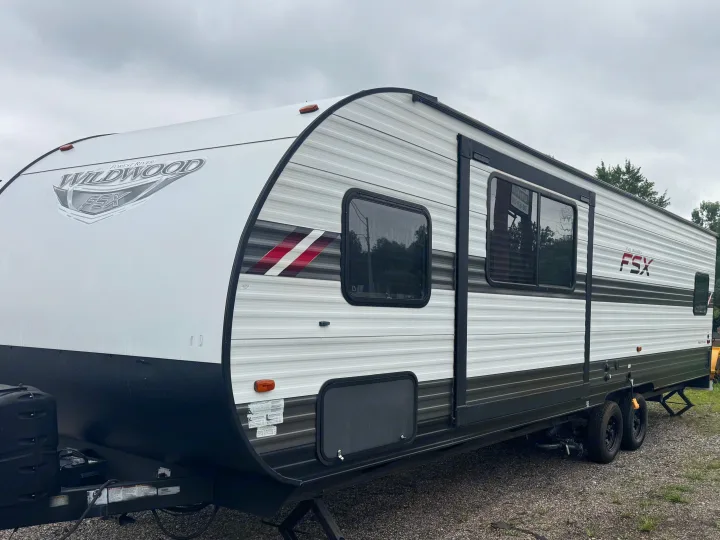 This Forest River Wildwood FSX travel trailer is ready for your next rv rental adventure, parked on gravel under a cloudy sky.. Forest River Wildwood FSX Toy Hauler 2021