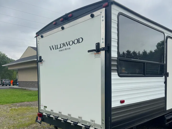 Rear view of a white Wildwood Forest River RV, showing its back door/ramp and side window, ready for an RV rental adventure.. Forest River Wildwood FSX Toy Hauler 2021