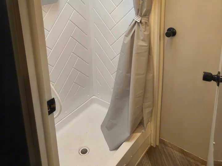RV rental shower: a white stall with herringbone walls, grey curtain, and drain visible on the compact floor. Functional and clean.. Forest River Wildwood FSX Toy Hauler 2021