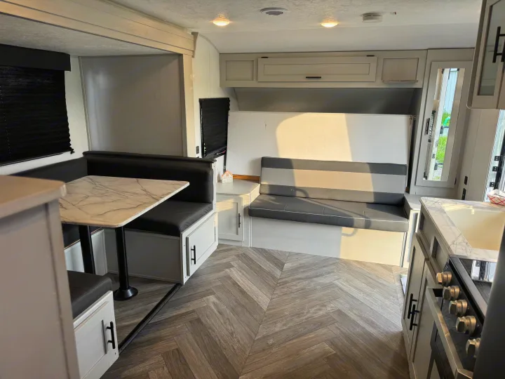 Inside this modern RV rental: a comfortable dinette, striped sofa, kitchenette, and stylish herringbone floor. Bright and inviting.. Forest River Wildwood FSX Toy Hauler 2021