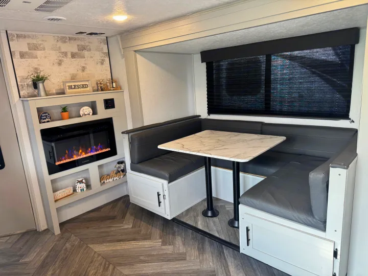 Cozy RV rental interior: modern dinette with marble table, U-shaped seating, electric fireplace & decor shelves.. Forest River Wildwood FSX Toy Hauler 2021