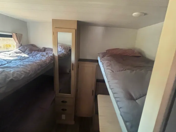 Inside this RV rental, find a comfortable bunk bed sleeping area with soft gray bedding and a central mirrored cabinet for convenience.. Forest River Evo 3005 2024