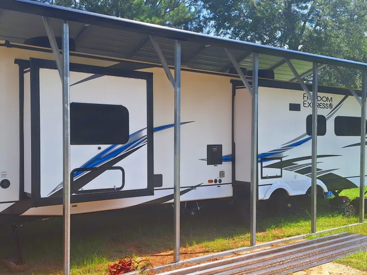 A white Freedom Express travel trailer, possibly an rv rental, is parked under a sturdy metal carport, offering outdoor protection.. Coachmen Liberty express 2021
