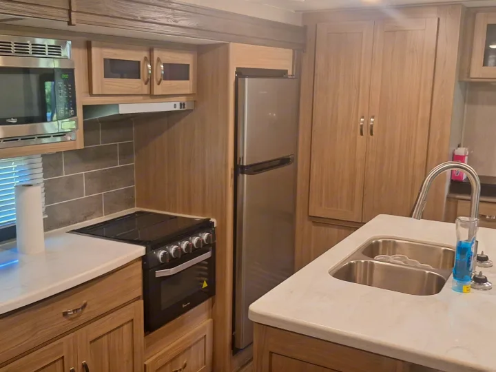 RV rental kitchen: This modern kitchen features light wood cabinets, stainless steel microwave, stove, refrigerator, & double sink.. Coachmen Liberty express 2021