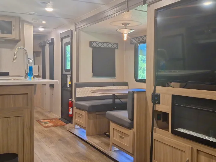 Modern RV rental interior: kitchen with sink, dining booth, and living area with TV & electric fireplace. Bright, wood-toned space.. Coachmen Liberty express 2021