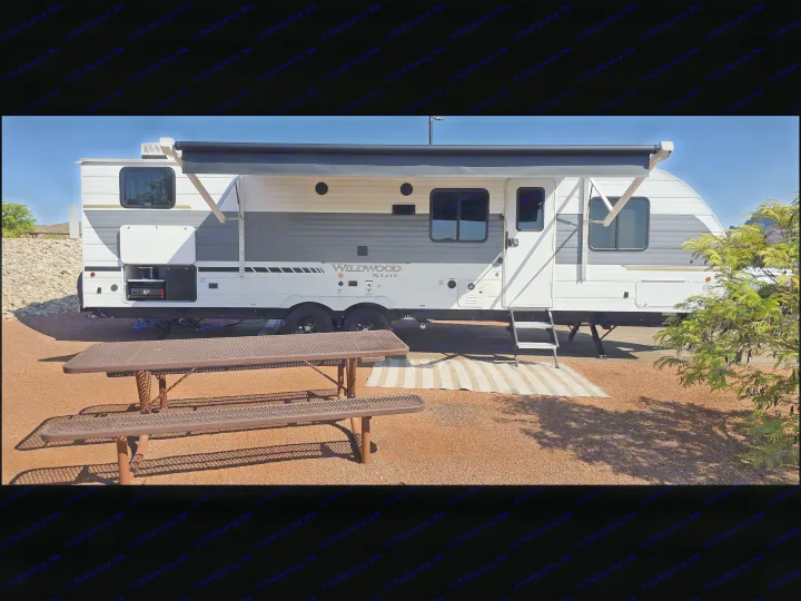 Wildwood X-Lite RV rental at a sunny campsite with a picnic table and extended awning, ready for outdoor living.. Forest River Wildwood X-Lite 2025