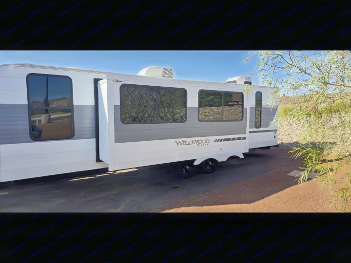 Wildwood X-Lite RV rental: A white & gray travel trailer with slide-out extended, parked on asphalt. Clear sky overhead.. Forest River Wildwood X-Lite 2025