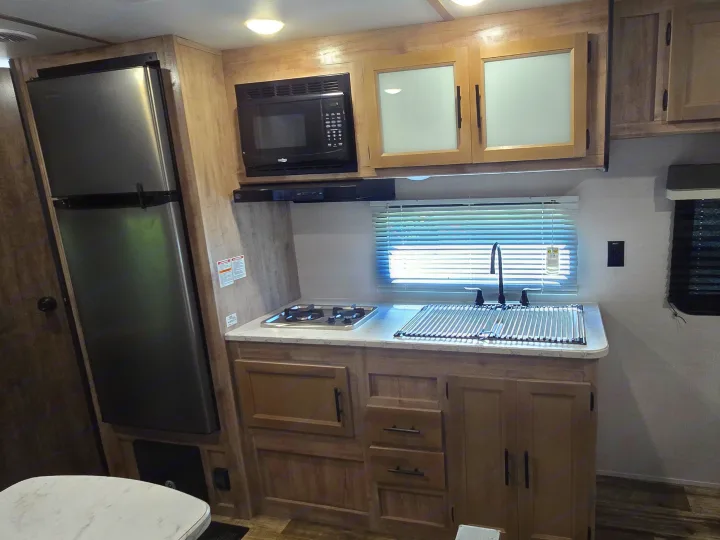 RV rental kitchen: stainless fridge, microwave, stovetop, sink with drying rack, and natural wood cabinets.. Gulf Stream Ameri-Lite 2024