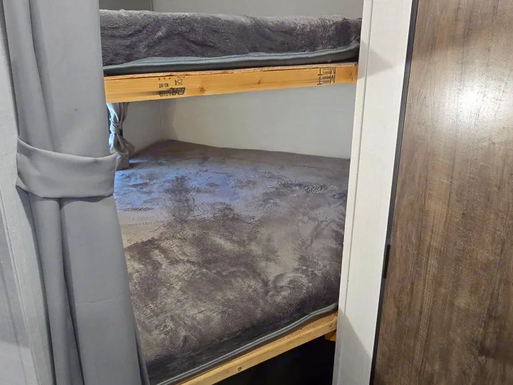 RV rental bunk beds with soft gray bedding and wooden frames, offering a cozy sleeping space for travel.. Gulf Stream Ameri-Lite 2024