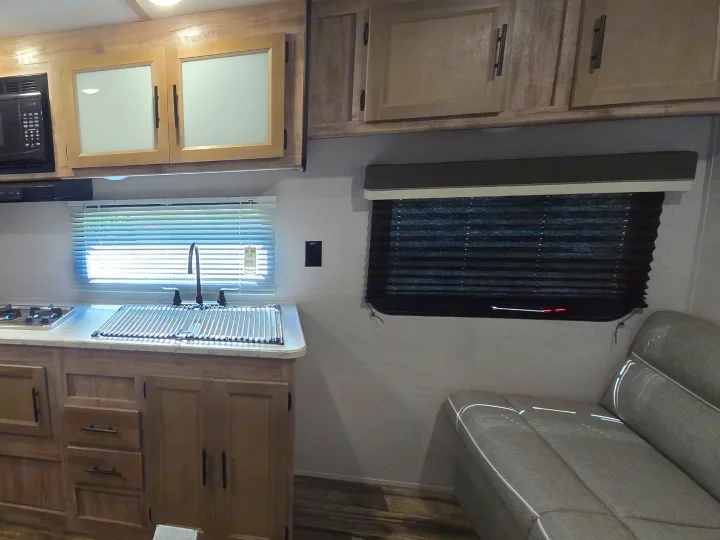 RV rental interior: A well-equipped kitchen area with a microwave, sink, and cabinets, next to a comfortable seating bench.. Gulf Stream Ameri-Lite 2024
