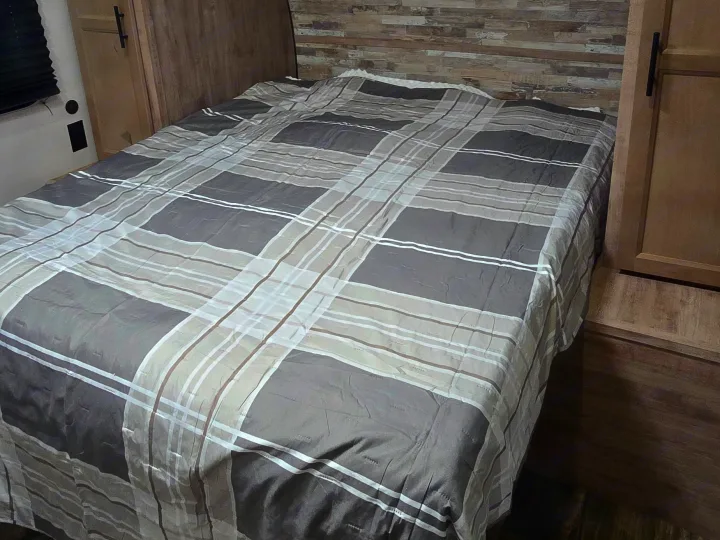 Experience comfort in this RV rental bedroom featuring a plaid comforter, compact design, and wood-paneled walls.. Gulf Stream Ameri-Lite 2024