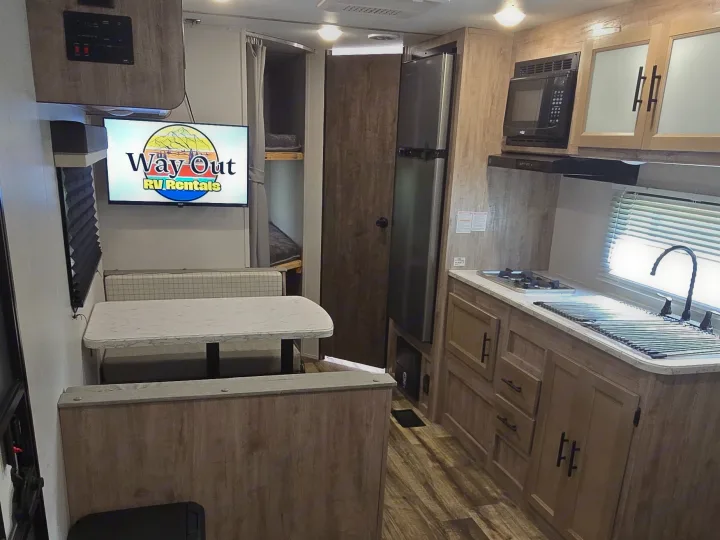 A cozy rv rental interior features a kitchen, dining booth, bunk beds, and a TV displaying "Way Out RV Rentals" logo.. Gulf Stream Ameri-Lite 2024
