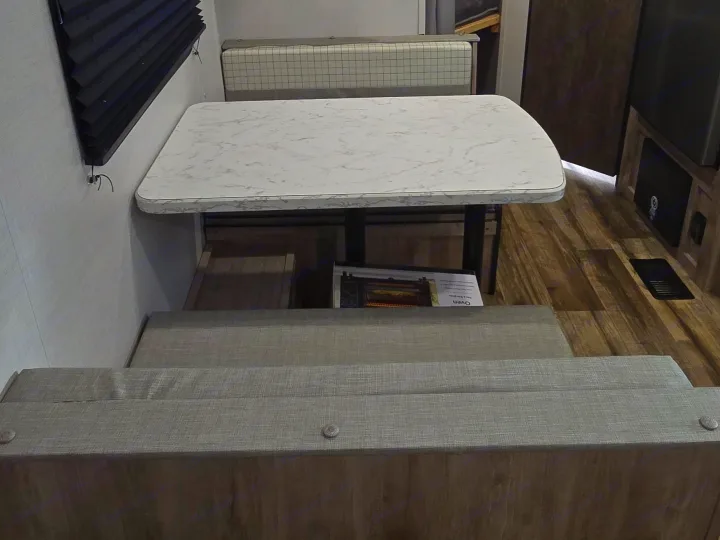 RV rental interior: dinette with marble-look table, grey booth seating, black blind, and steps to a lower level.. Gulf Stream Ameri-Lite 2024