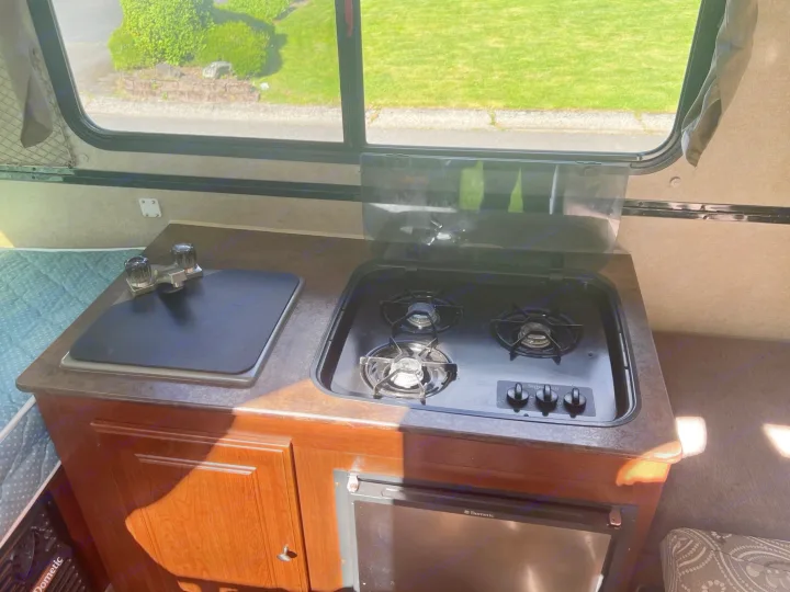 Enjoy a functional rv rental kitchen: a compact galley with a sink, 2-burner stove, Dometic fridge, and a scenic window view.. Forest River Rockwood Premier 2015