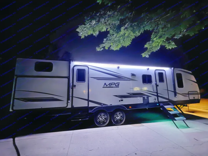 Modern rv rental travel trailer illuminated by LED lights at night, with steps extended, parked on concrete.. Cruiser RV MPG Ultra Lite 2022