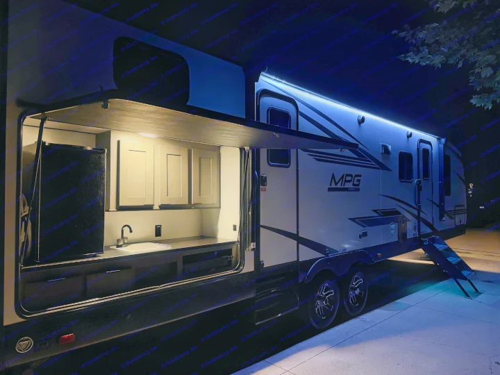 Nighttime view of a modern RV rental with an illuminated outdoor kitchen and blue LED awning lights for ultimate camping comfort.. Cruiser RV MPG Ultra Lite 2022