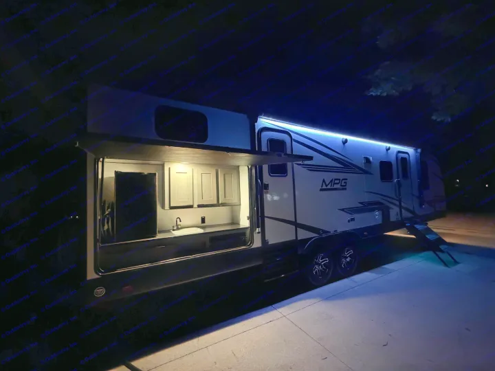 Night shot of an rv rental with an outdoor kitchen, sink, and cabinets illuminated by internal and blue LED strip lights.. Cruiser RV MPG Ultra Lite 2022