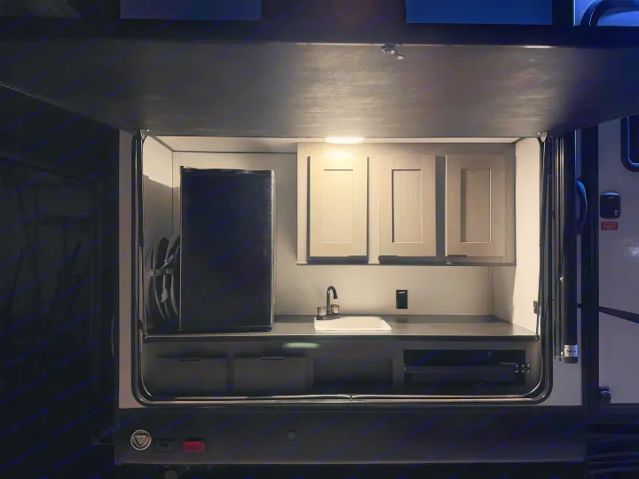 Brightly lit outdoor kitchen in an RV rental, featuring a compact fridge, sink, and cabinets for convenient camping adventures.. Cruiser RV MPG Ultra Lite 2022