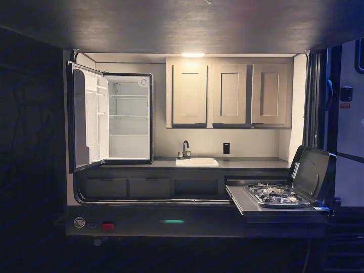 Explore this rv rental's outdoor kitchen: open mini-fridge, sink, overhead cabinets, and a pull-out gas stove, ready for camping.. Cruiser RV MPG Ultra Lite 2022