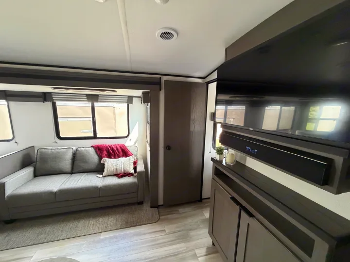 Cozy RV rental living room featuring a gray couch with accent pillows, a wall-mounted TV with soundbar, and wood-look flooring.. Cruiser RV MPG Ultra Lite 2022