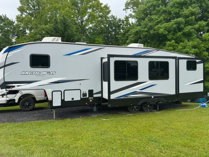 Spacious grey Arctic Wolf Cherokee rv rental with blue stripes, slide-outs extended, parked in a lush campground setting.. Forest River Cherokee Arctic Wolf 2022